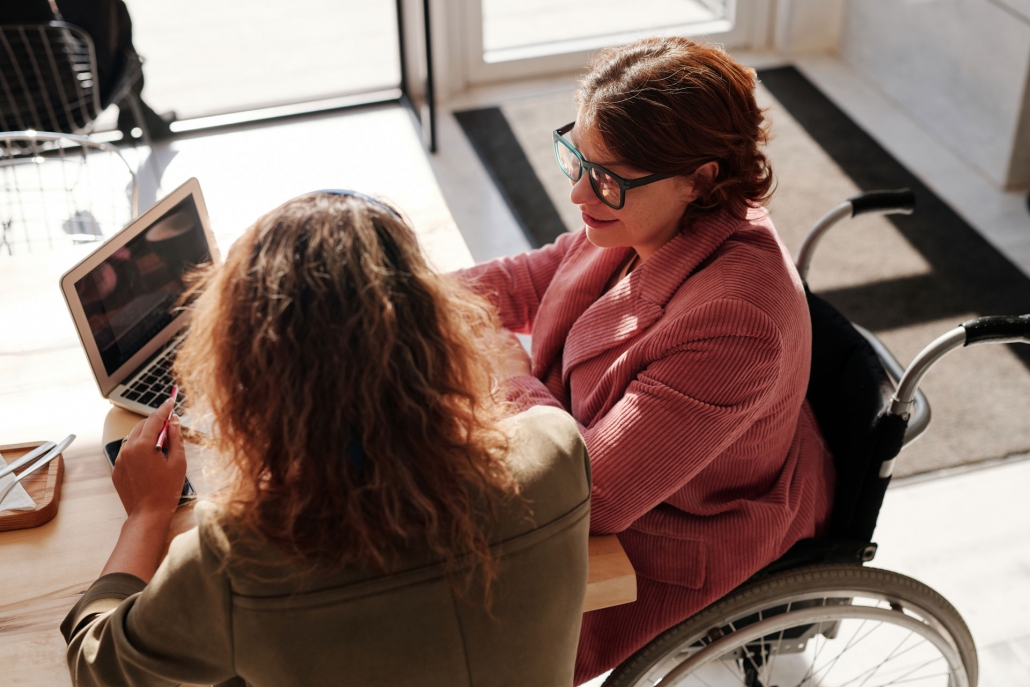 woman in red sweater wearing black framed eyeglasses sitting with support coordinator of the NDIS who is helping her with her NDIS plan